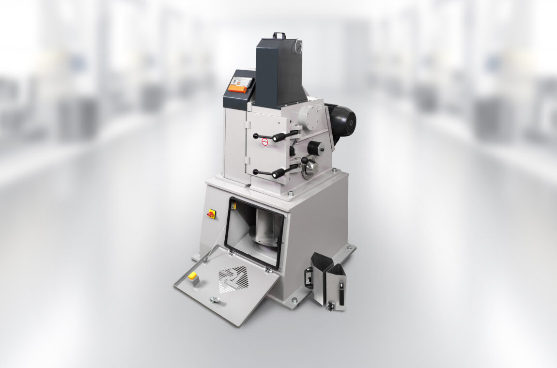 Single-toggle crusher / jaw crusher EB150x100 TL in the laboratory. The device's grinding chamber is open, 2 sub-units are next to the device. The smartphone with app control is switched on and ready for operation