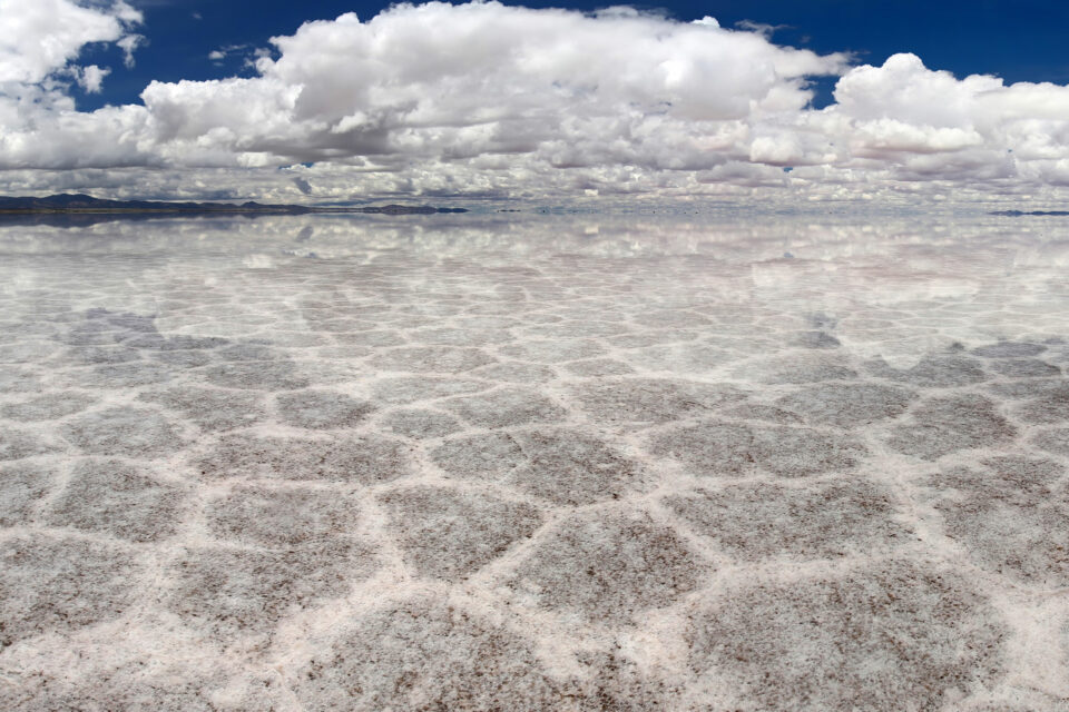 Photo of a salt lake with a blue sky, clouds reflected in the water and mountains in the background