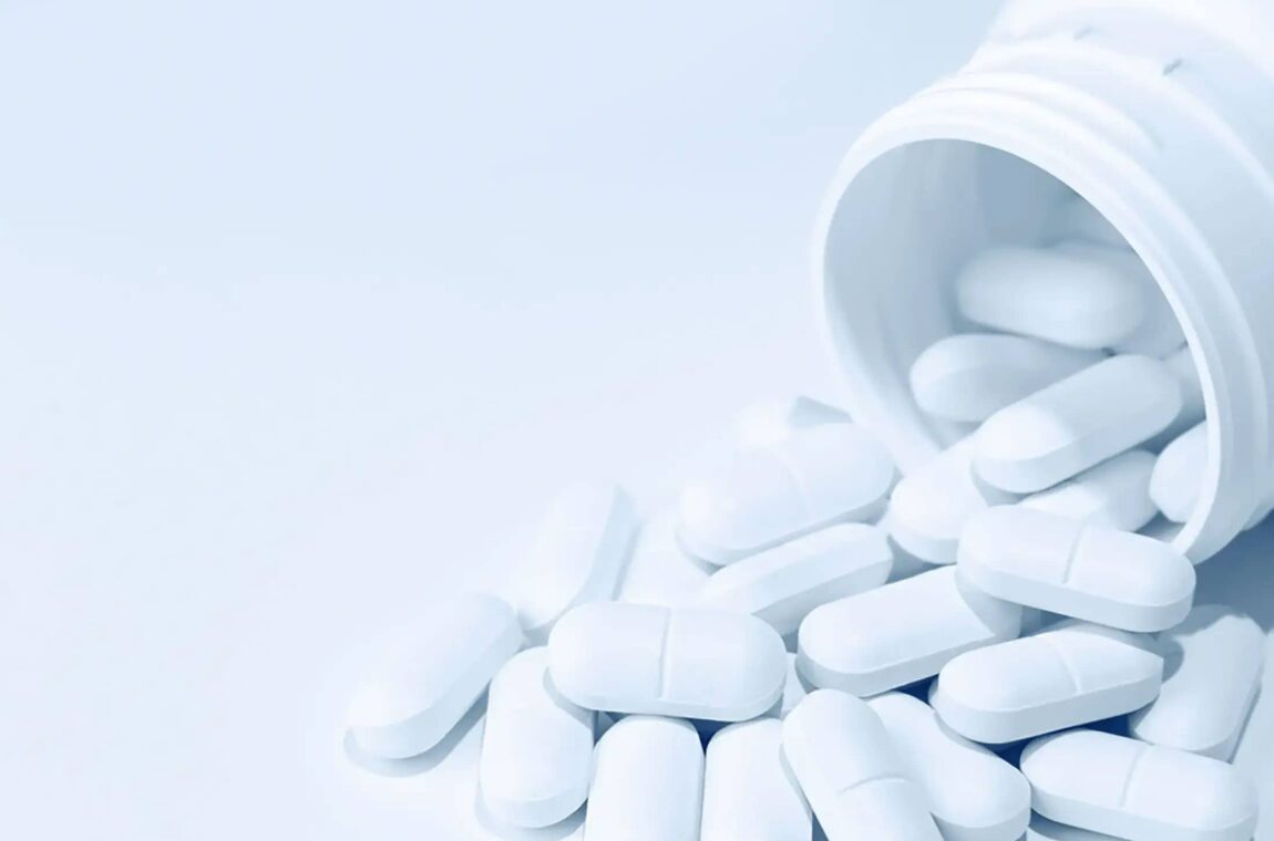 Applications: Pharmaceuticals: Tablet tin lying on its side, a small quantity of white tablets with a broken notch has fallen out of the tin and is lying in the opening